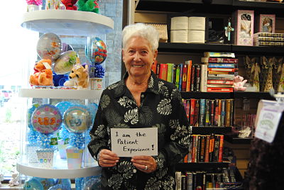 This is a picture of a older female smiling and holding a sign that says:
&quot;I am the patient Experience!&quot;