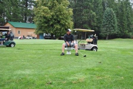 Picture of a male golf player sitting on a bench outside surrounded by other golfers