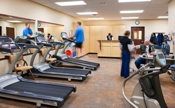 Picture of a male Patient on a treadmill and a female Nurse helping older male patient that is sitting down in The Pulmonary Rehabilitation Program Gym