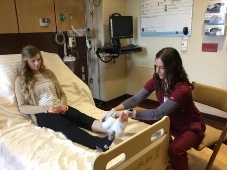 Picture of a female patient lying in bed while a female nurse wraps her foot in bandage