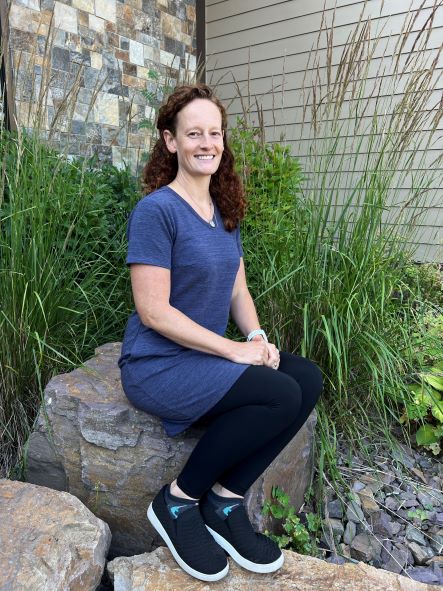 Carrie Wardian, Pediatric PT, sitting outside on a rock.