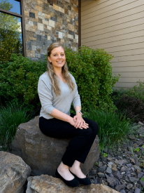Emergency Medicine Physician Dr. Katelynn Bailey, sitting outside of the Hospital, on a rock, and smiling