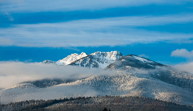 Picture of a snowy mountain with the clouds touching the tip and a blue sky